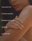 Close up of a woman smoothing body cream onto their upper arm. Text reads: Vegan and cruelty-free. 100% Natural Fragrance. No parabens or phthalates. Sulfate-free. For all skin types.